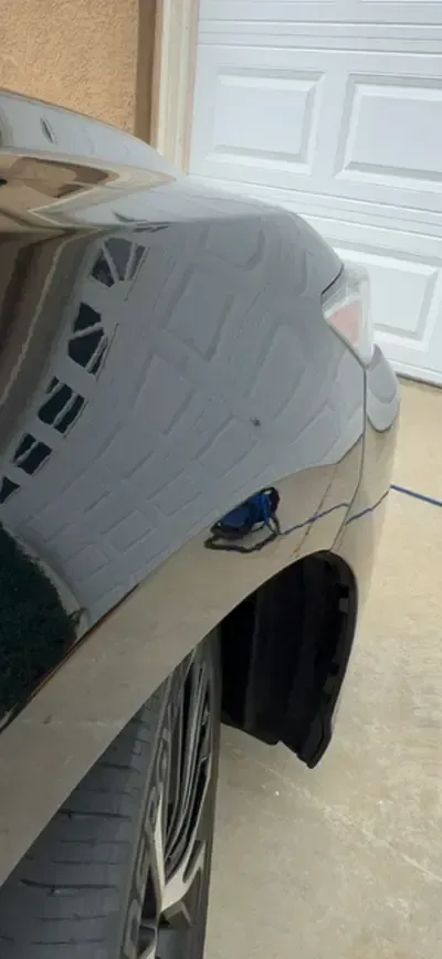 Black car's rear quarter panel reflecting a white garage door and part of a tire and wheel.