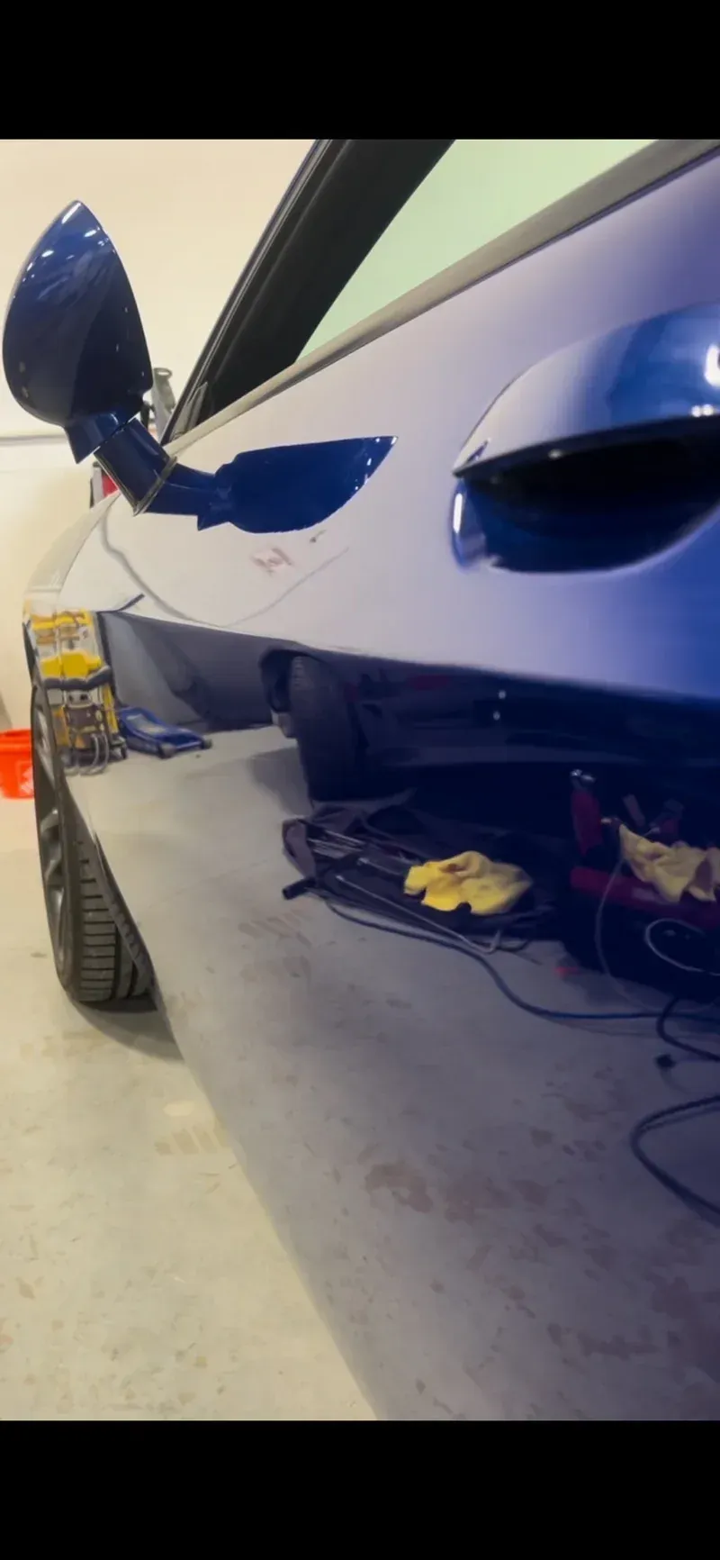 Blue car body with side mirror extended, resting on a gray surface in a garage.