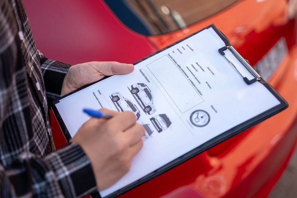 Person holding a clipboard, writing, next to a red car.
