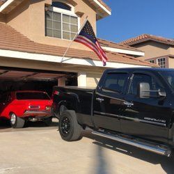 Black pickup truck parked in front of a house with American flag. A red car is in the open garage.