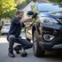 Man in dark blue shirt and gloves inspecting a black SUV tire on a residential street.