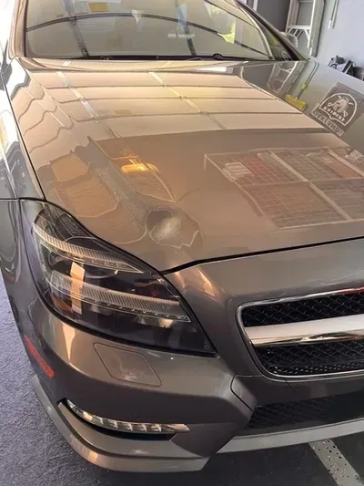 Gray Mercedes-Benz car with prominent headlights, front grill, and reflecting ambient light.