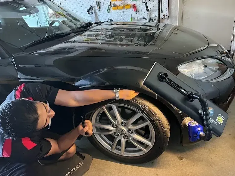 Person using a tool on a red car to fix a dent.