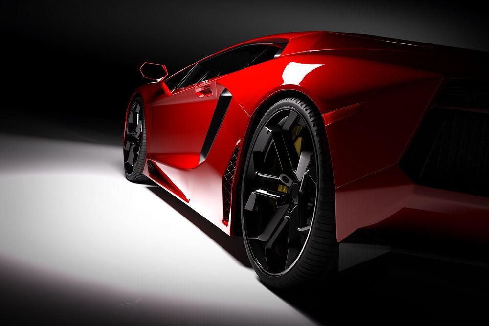 Red sports car, glossy finish, rear view angled towards a spotlight, black wheels.