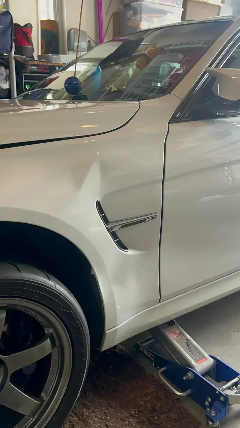 White car on a jack in a garage, fender dented near the side vent.