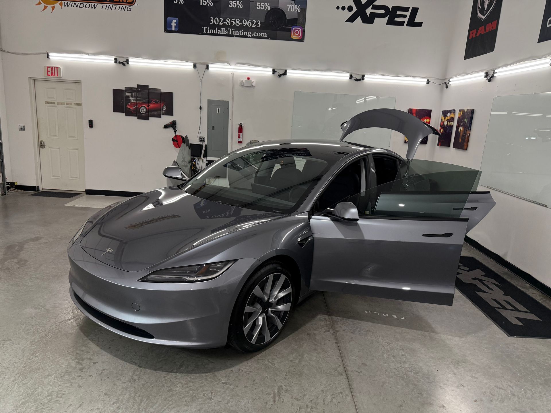A gray tesla model 3 is parked in a garage with its doors open.