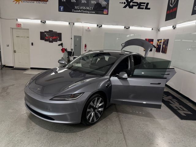 A gray tesla model 3 is parked in a garage with its doors open.