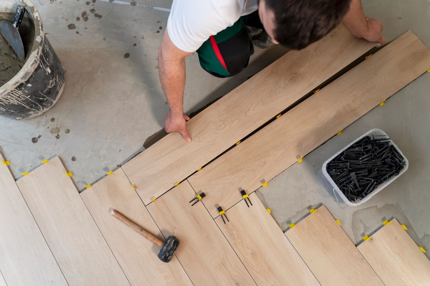 Person installing wood-look tile flooring, using spacers and a mallet.