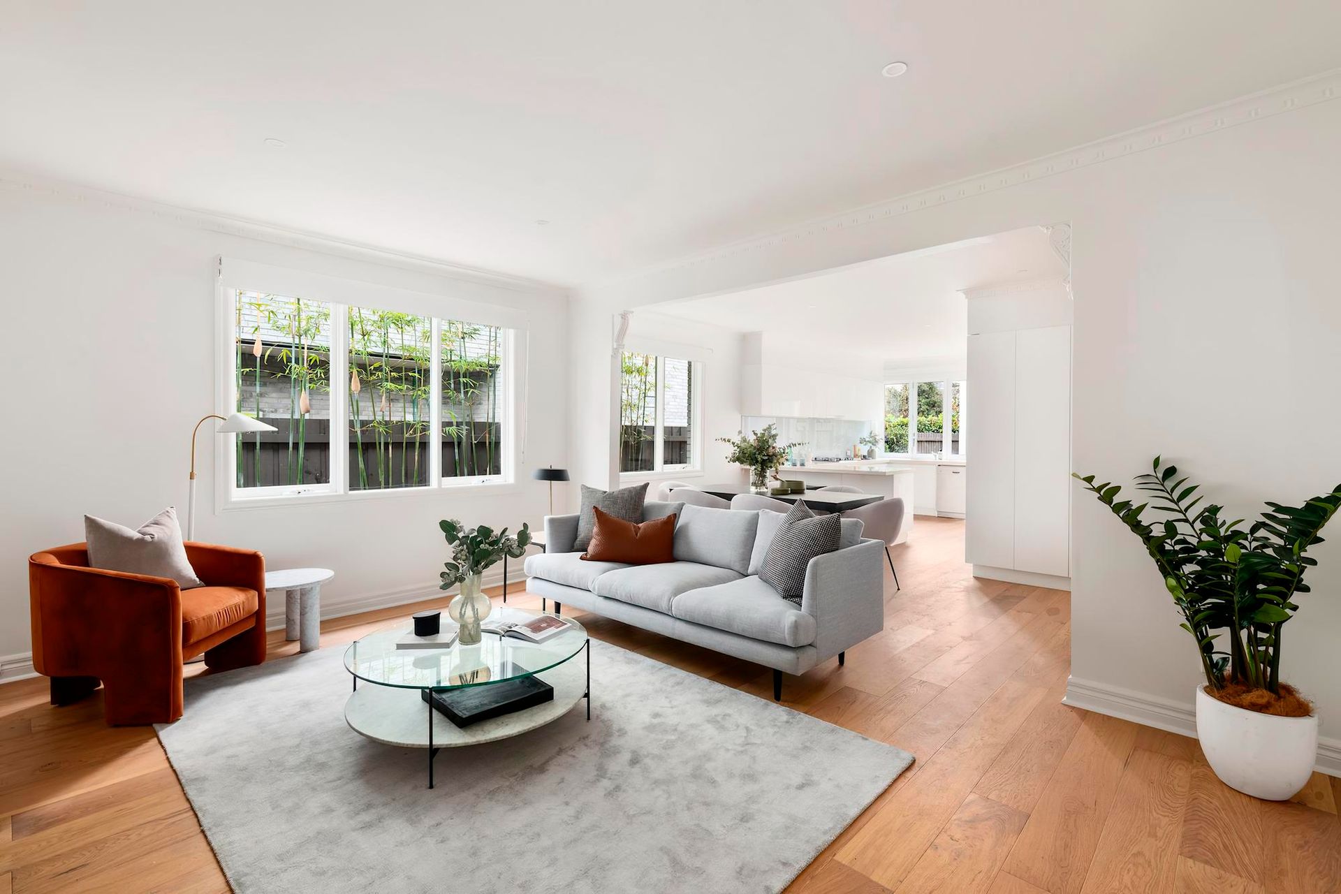 Living room with light gray sofa, orange chair, glass coffee table, and open doorway to kitchen.