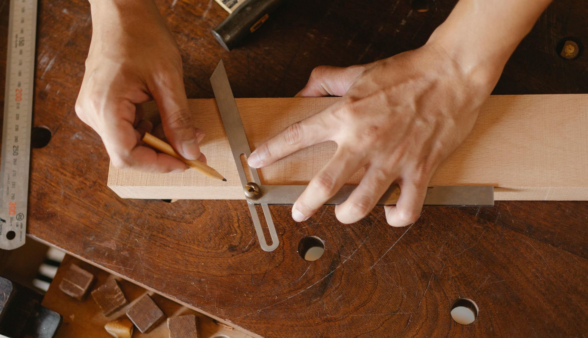 Hands using a bevel gauge and pencil to mark wood on a workbench.