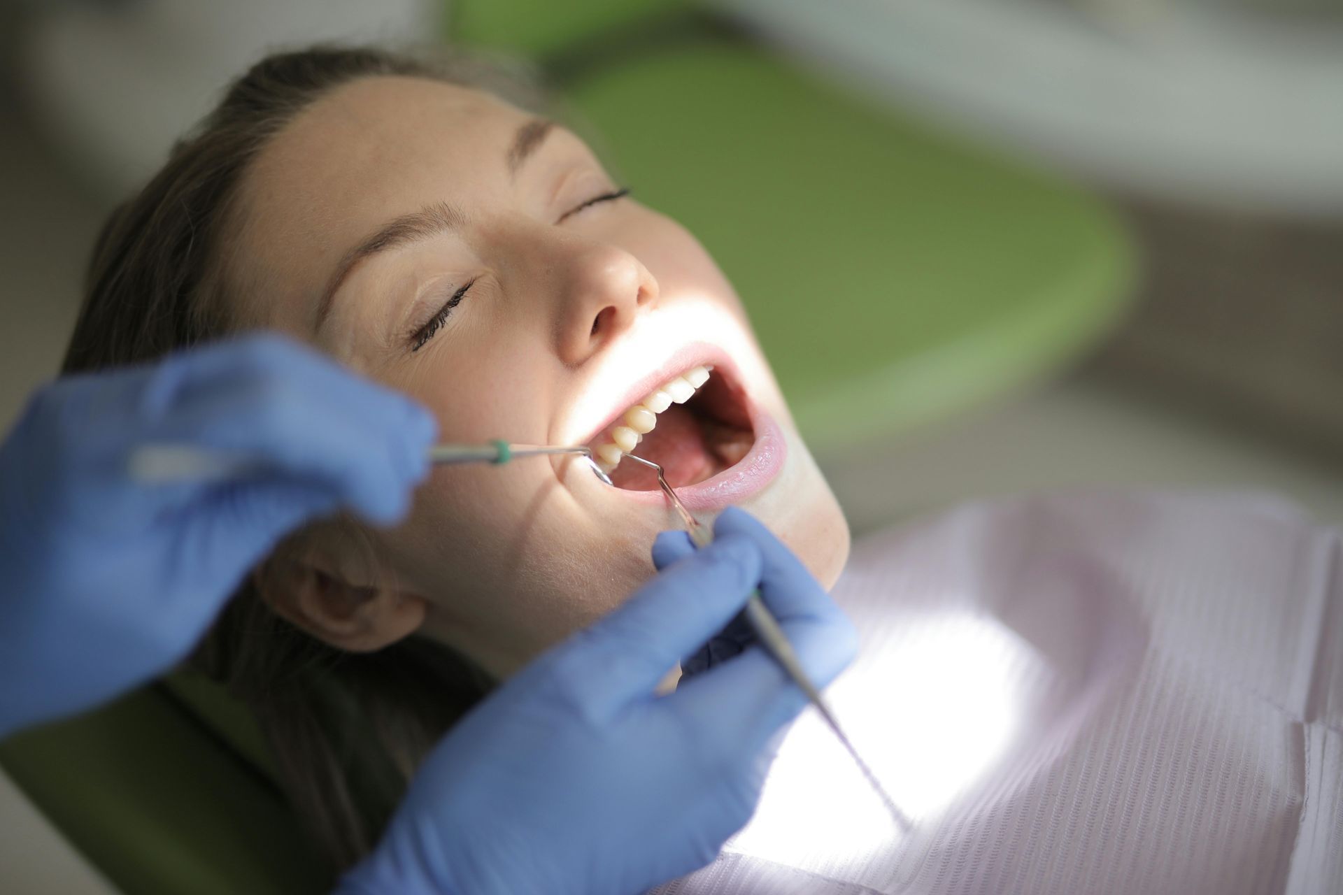 Persona sulla poltrona del dentista con la bocca aperta, dentista che utilizza degli strumenti.