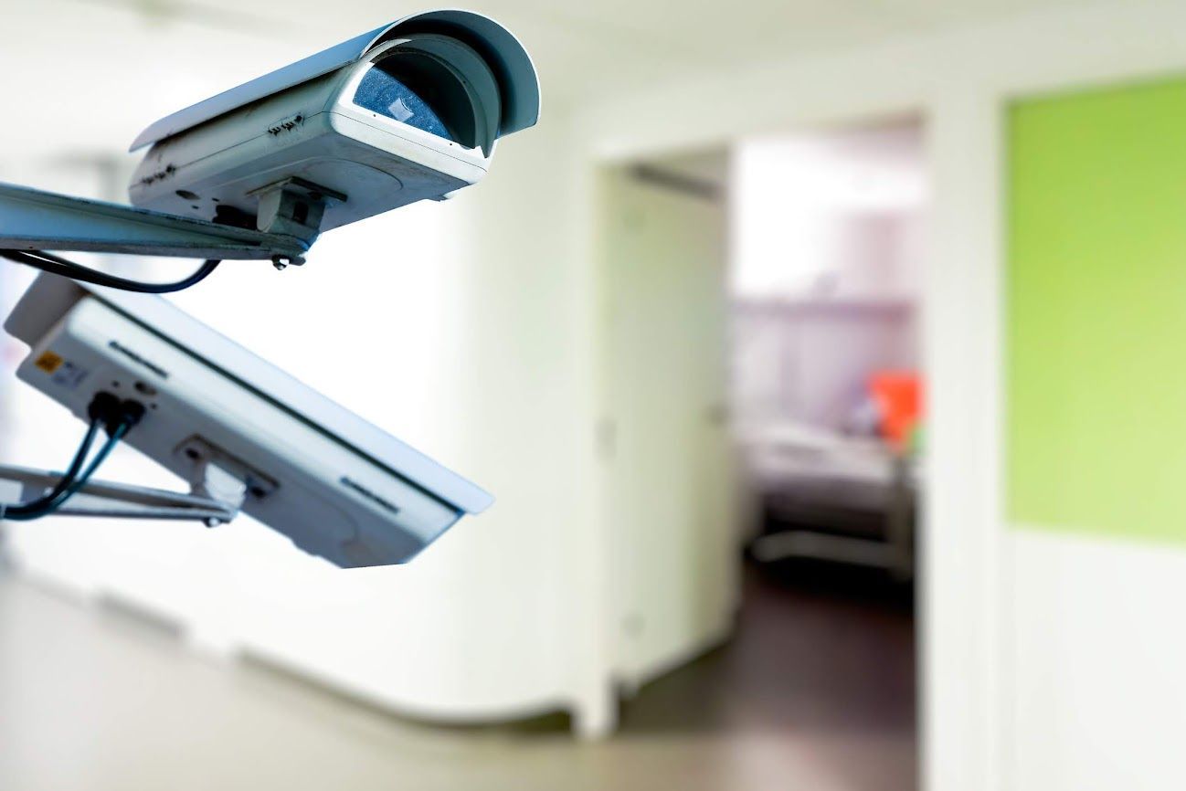 Due telecamere di sicurezza montate su una parete sorvegliano un corridoio con sfondo sfocato.