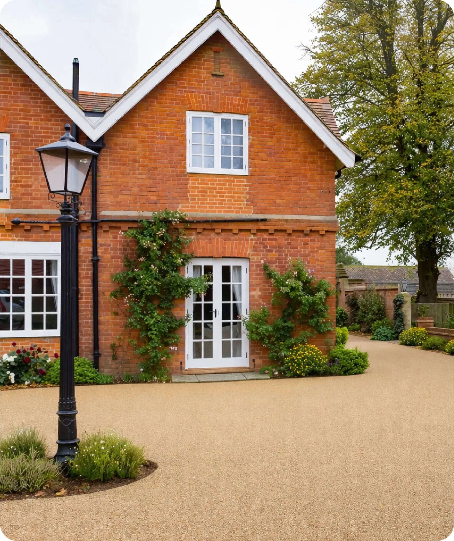 A red brick house with a white trim gable, a set of French doors, and a decorative lamp post on a gravel driveway.