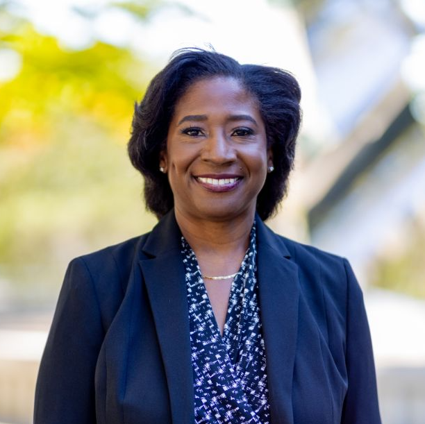 A woman in a black jacket and floral shirt smiles for the camera