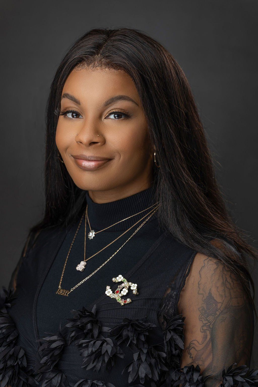 A young woman wearing a black dress and necklaces is smiling for the camera.