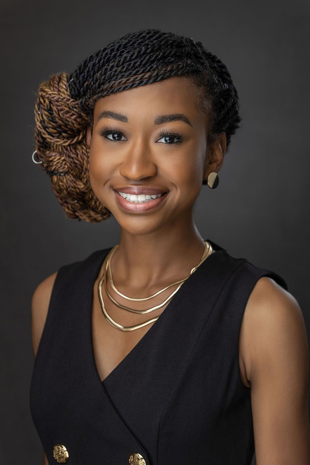 A woman wearing a black dress and a gold necklace is smiling for the camera.