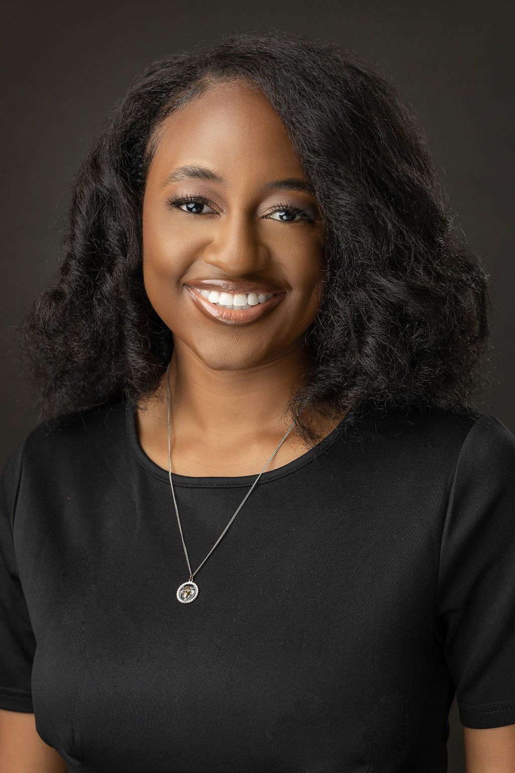 A woman wearing a black shirt and a necklace is smiling for the camera.