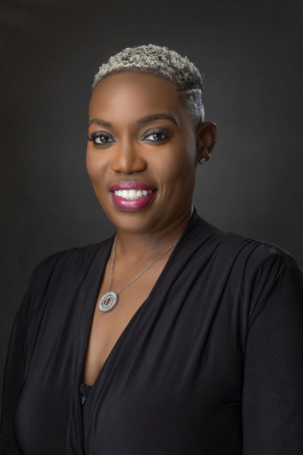 A woman in a black dress and necklace is smiling for the camera.