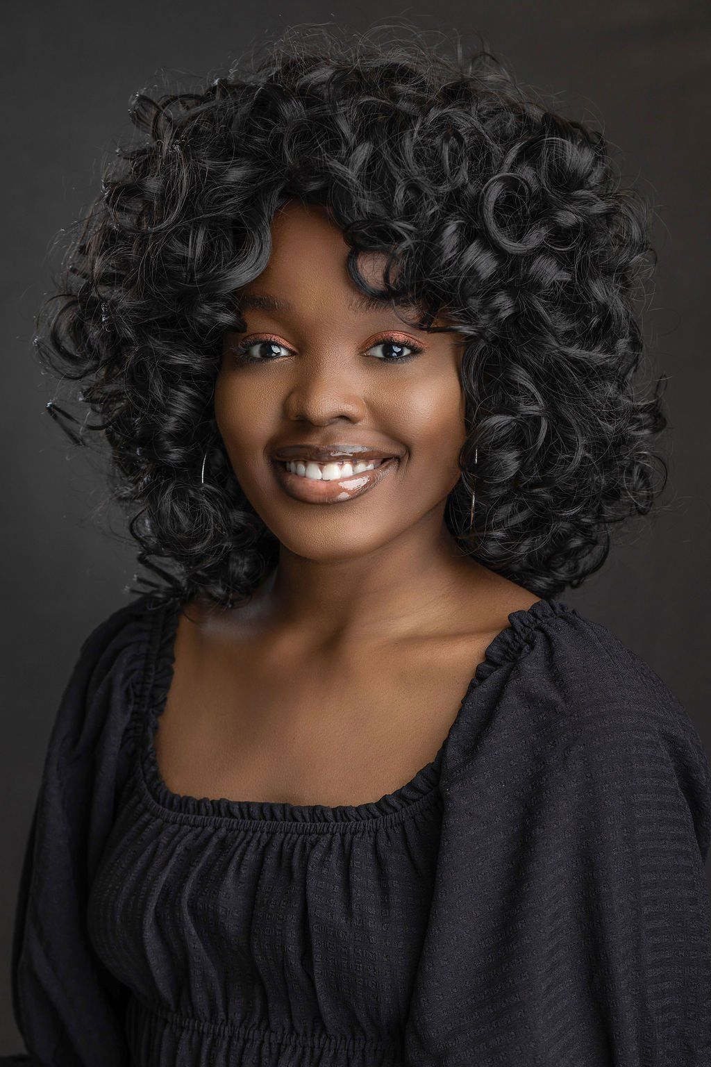 A woman with curly hair is smiling and wearing a black shirt.