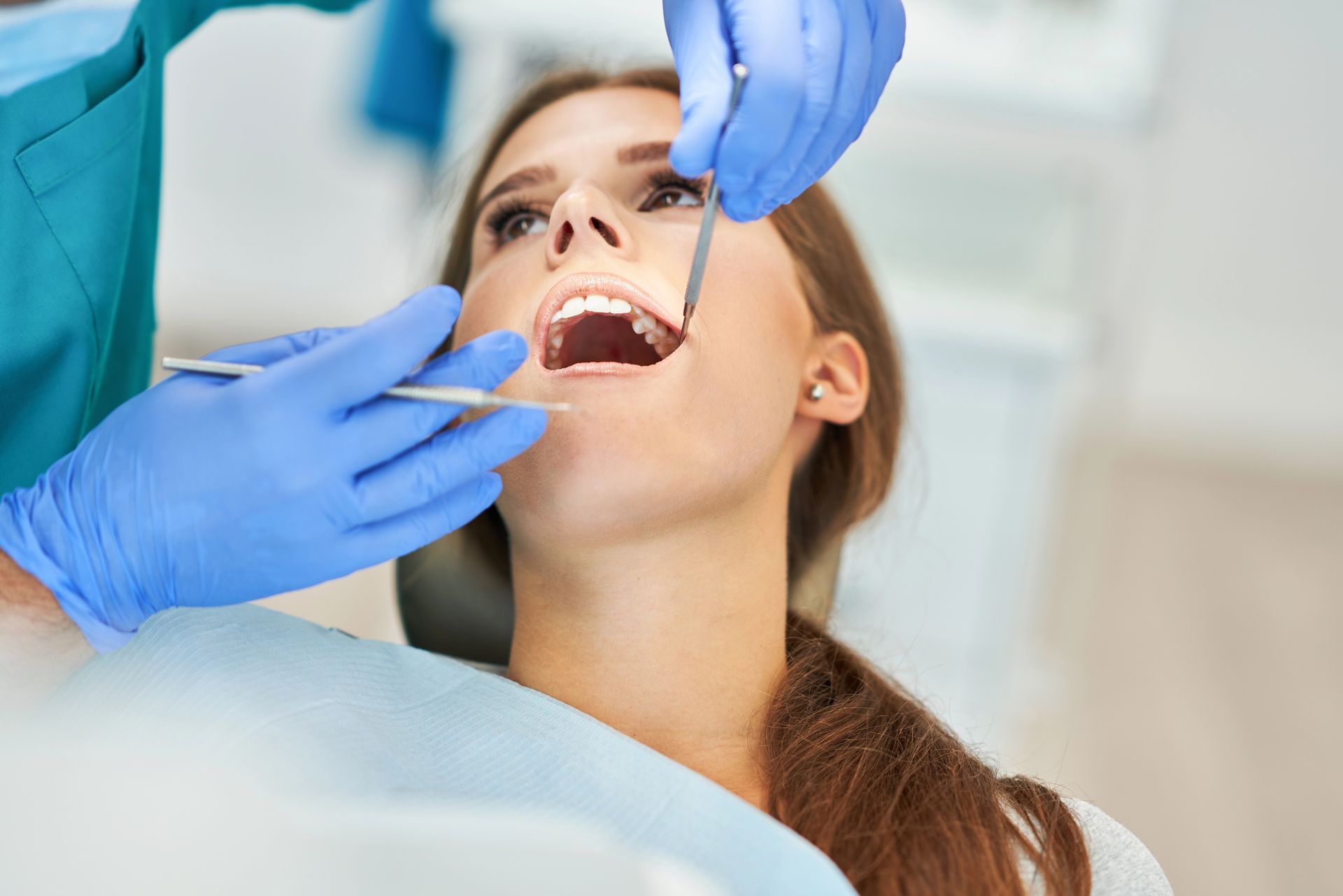 Un dentista con indosso guanti blu utilizza strumenti odontoiatrici per esaminare i denti di un paziente seduto su una poltrona.