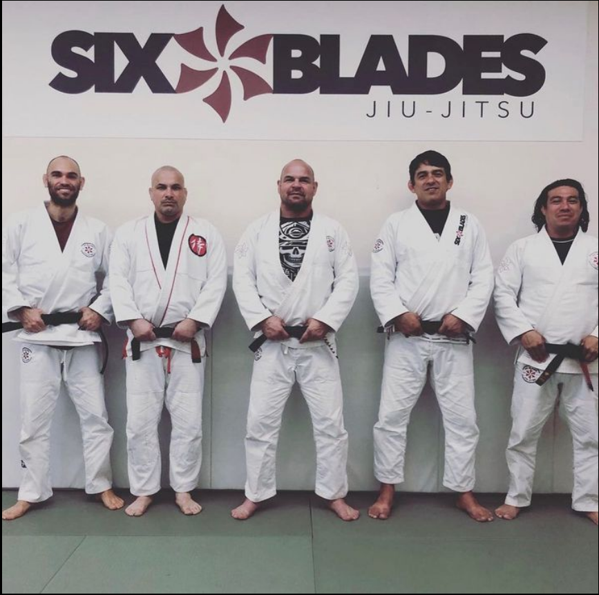 Five men in white Jiu-Jitsu gis stand in front of a