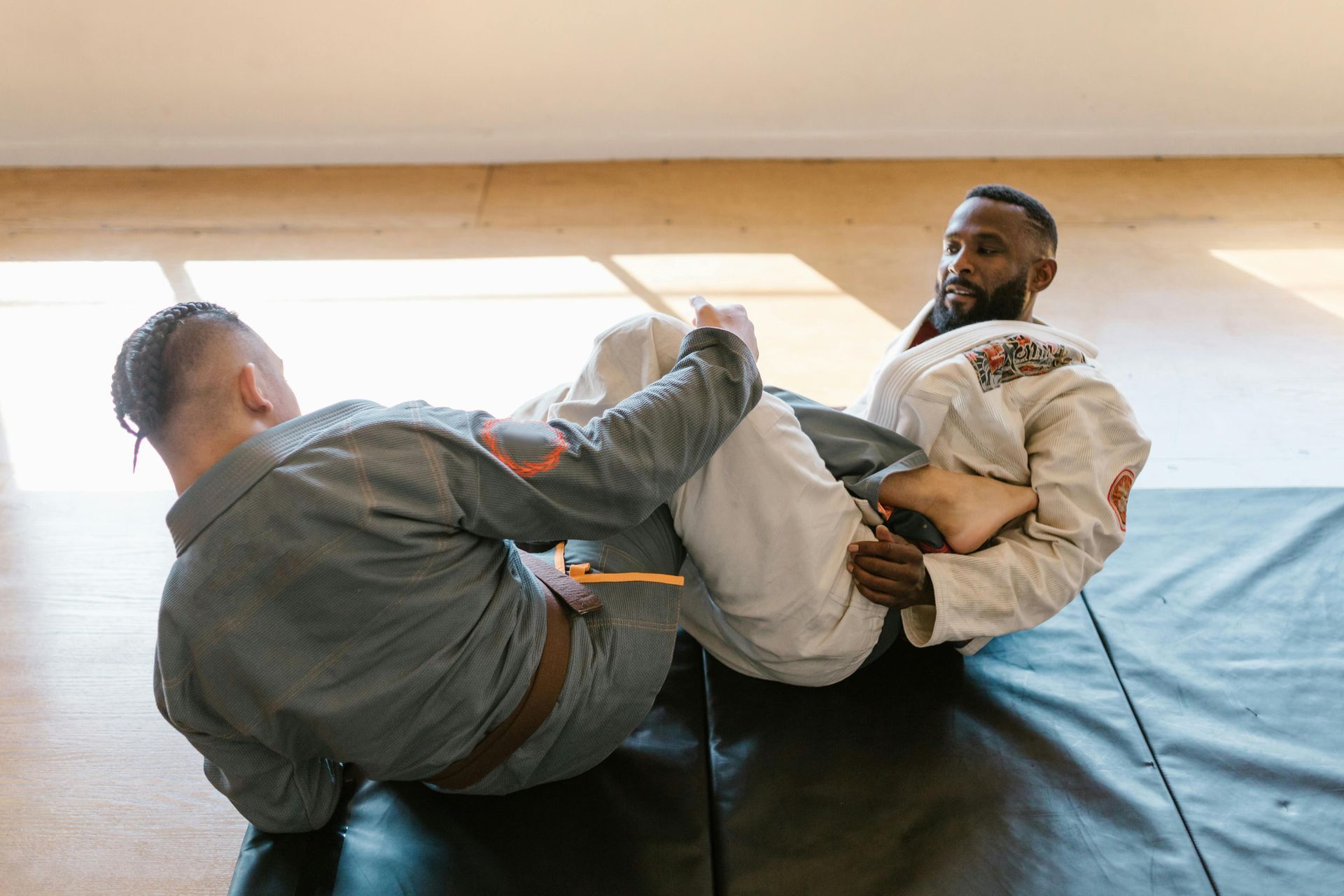 Two men are wrestling on a mat in a gym with one doing a heel hook on the other.