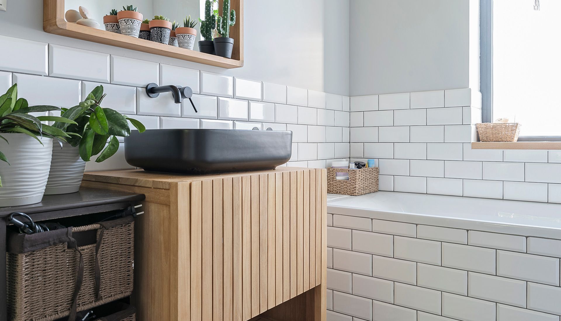 A bathroom with white tiles , a wooden vanity , a sink and a mirror.