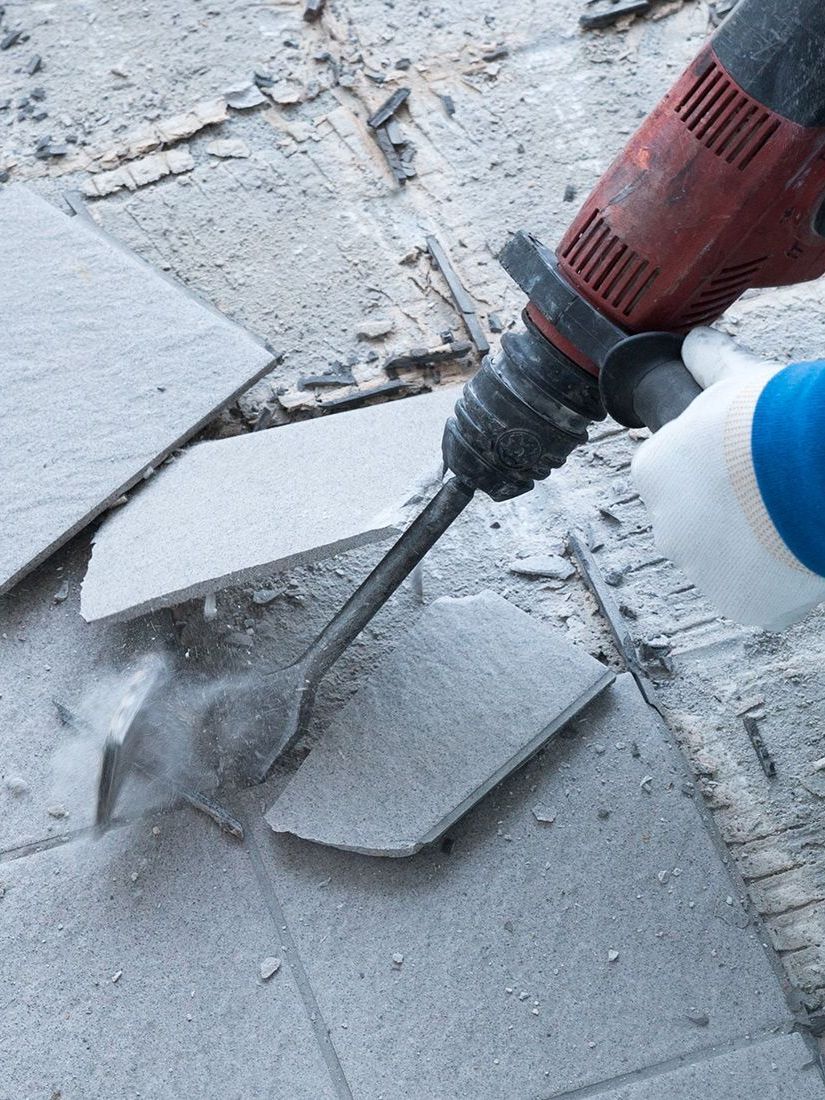 A person is using a hammer to break tiles on the floor.