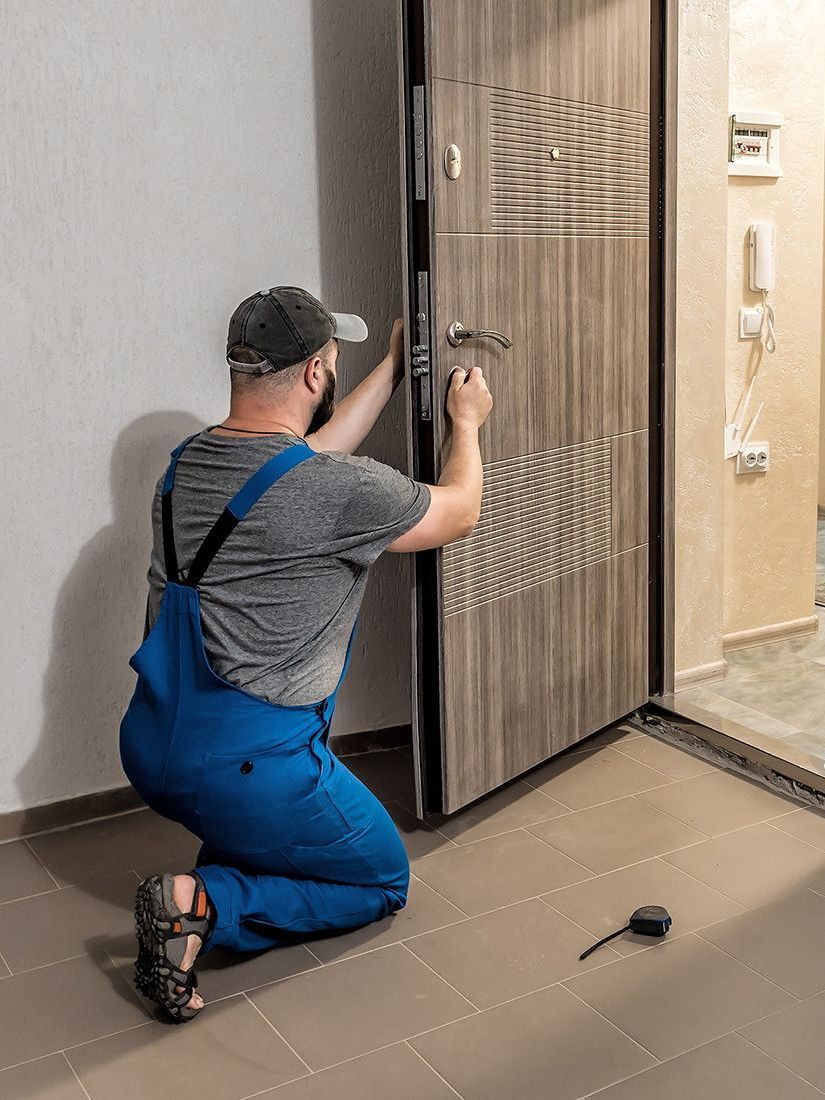A man is kneeling down to fix a door.