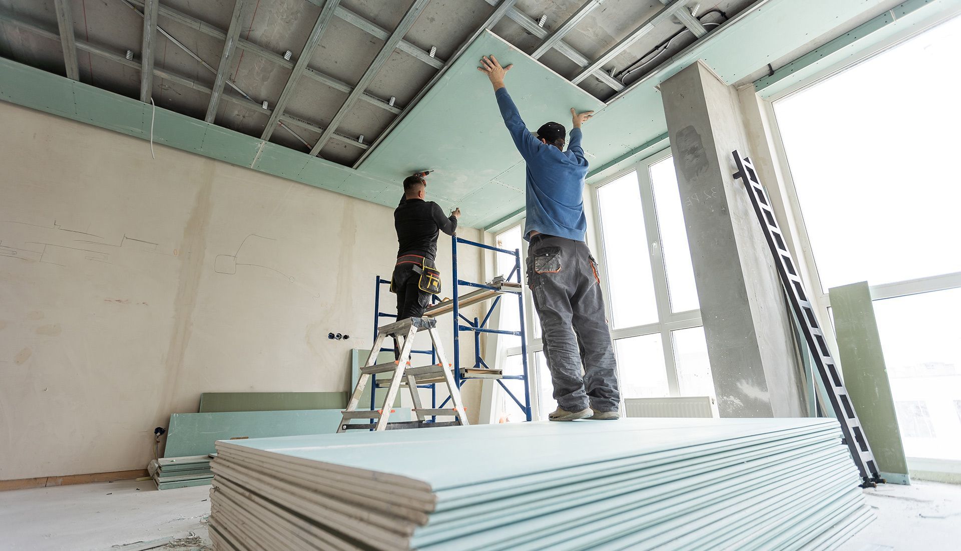 Two men are working on a ceiling in a room.