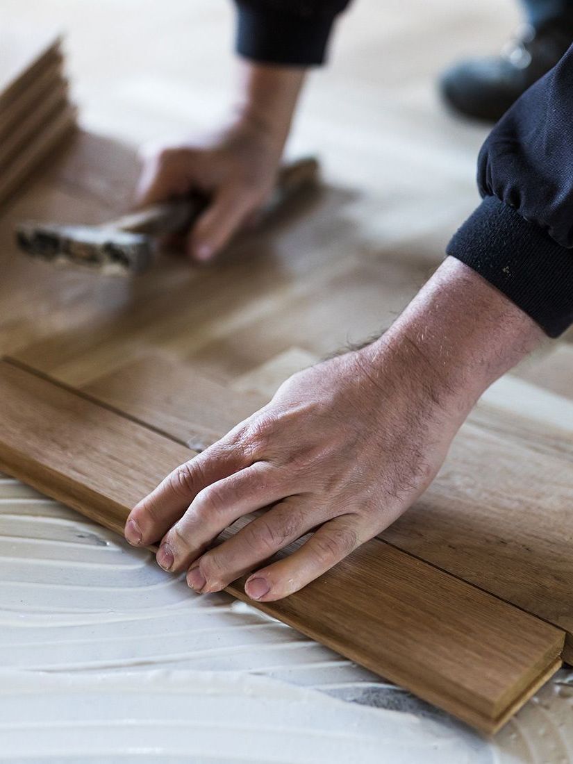 A person is installing a wooden floor with a hammer.