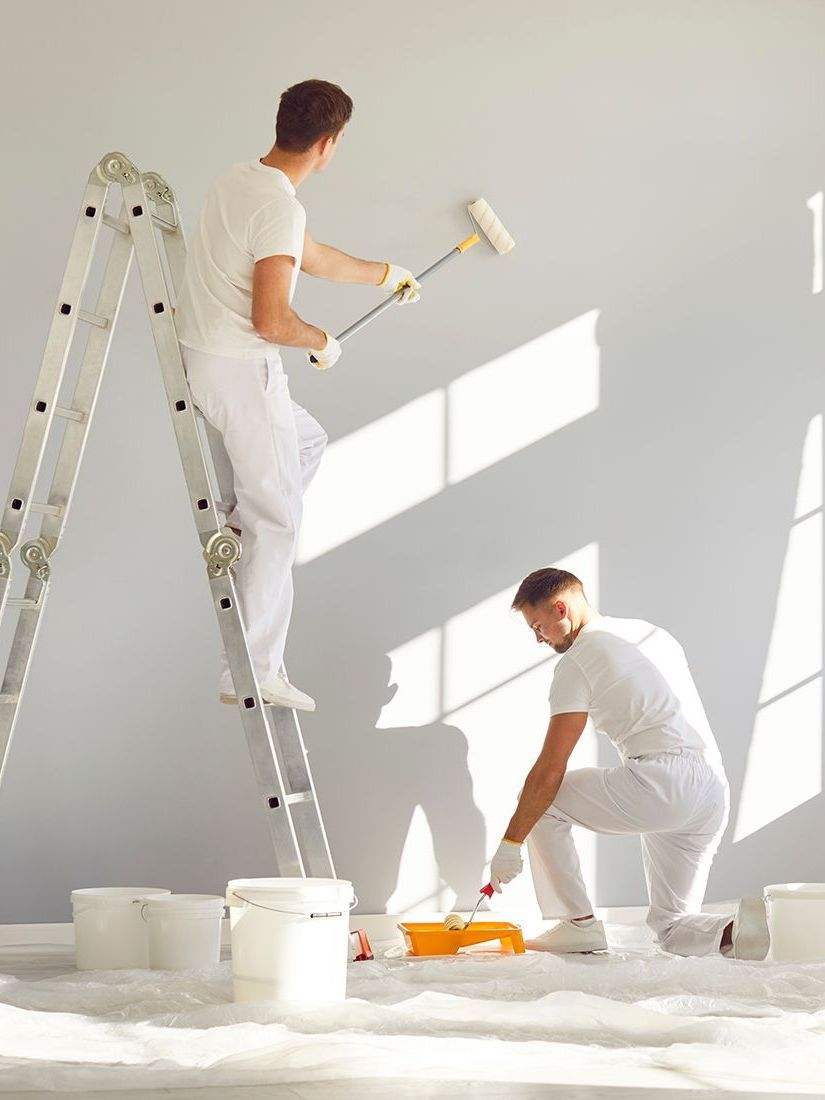 Two men are painting a wall in a room.
