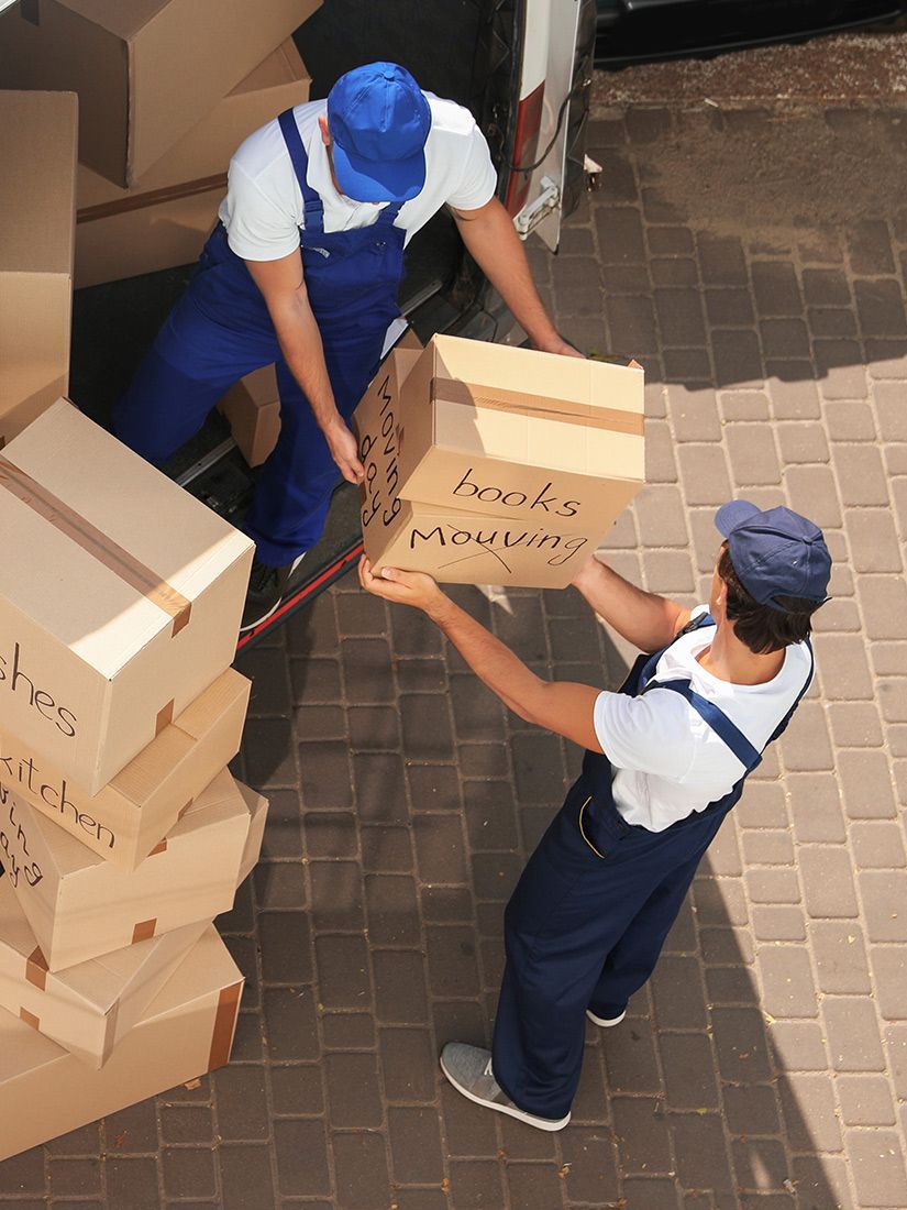 Two men in blue overalls are loading boxes into a truck