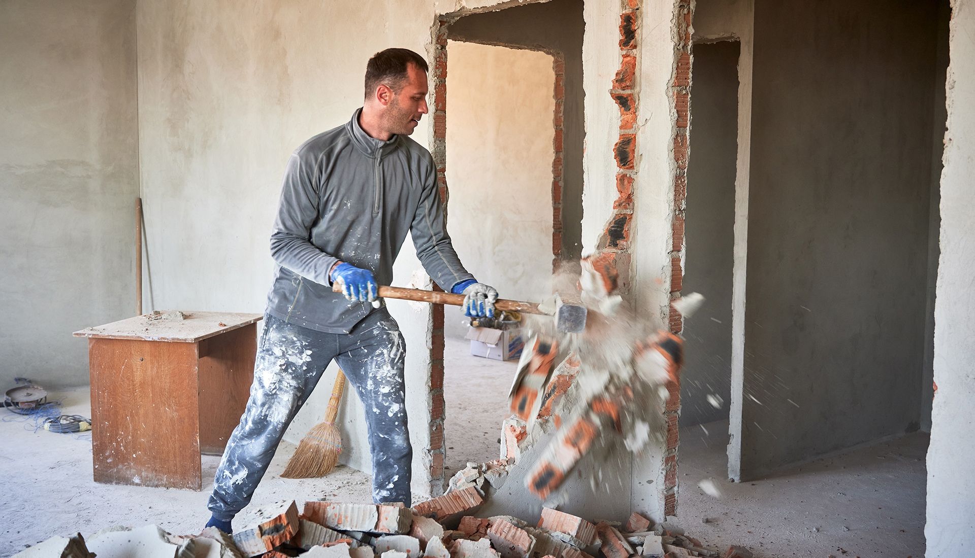 A man is breaking a brick wall with a hammer.