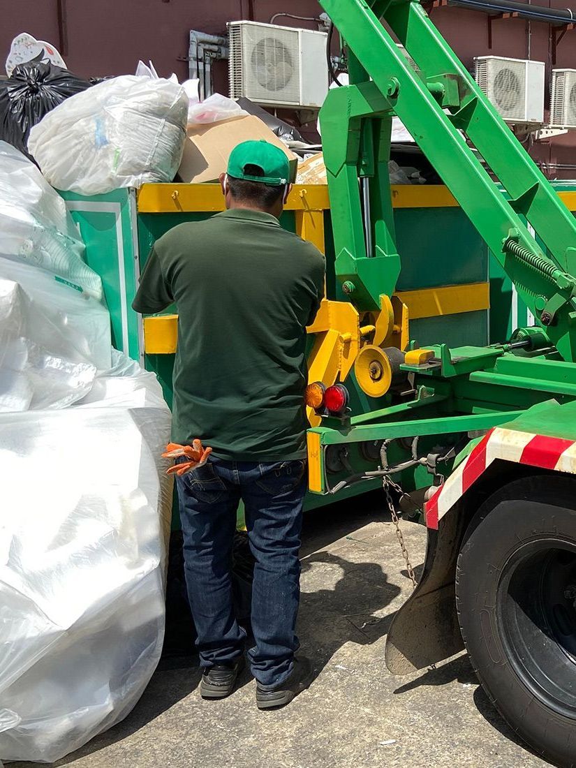 A man is standing in front of a green garbage truck.