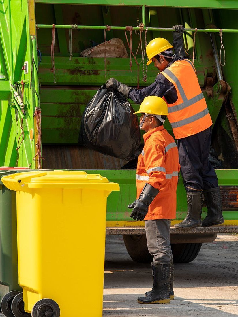 Two men are loading garbage into a garbage truck.