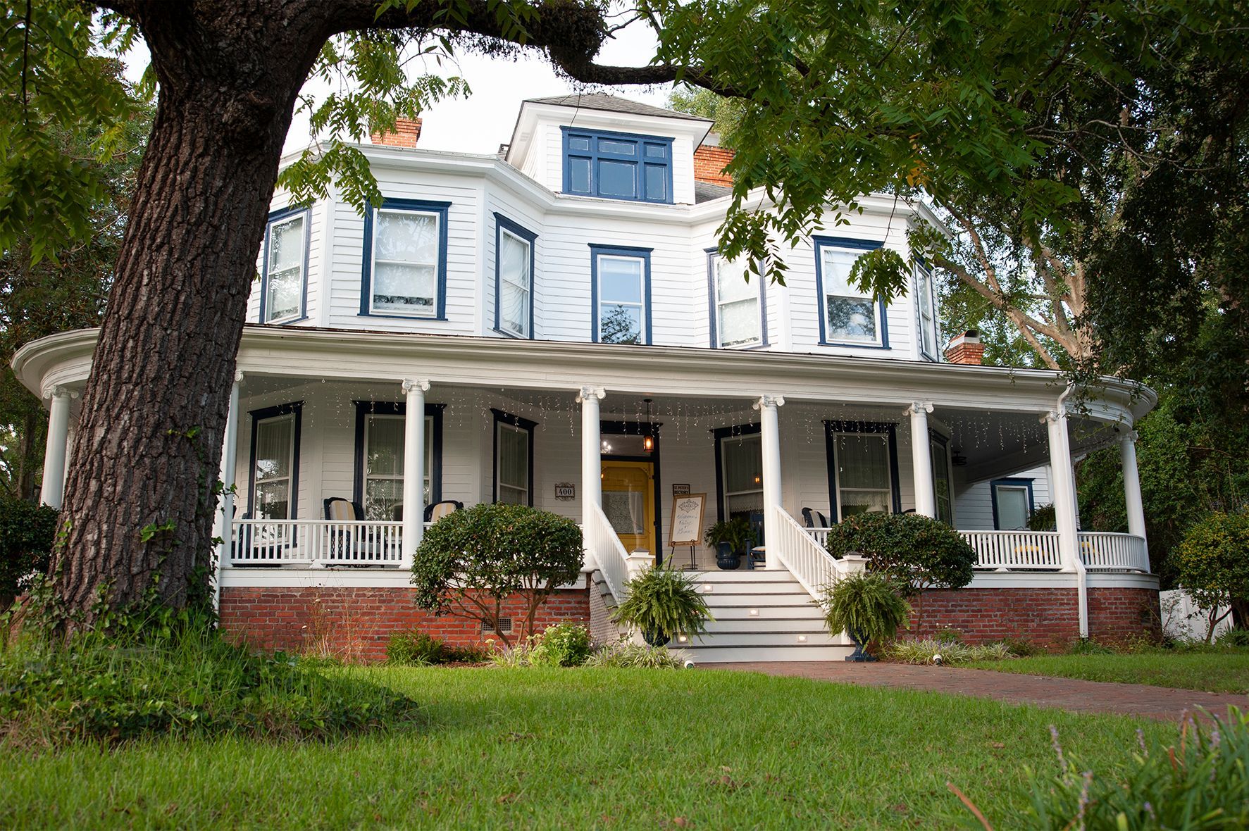 A large white house with a porch and purple flowers in front of it.