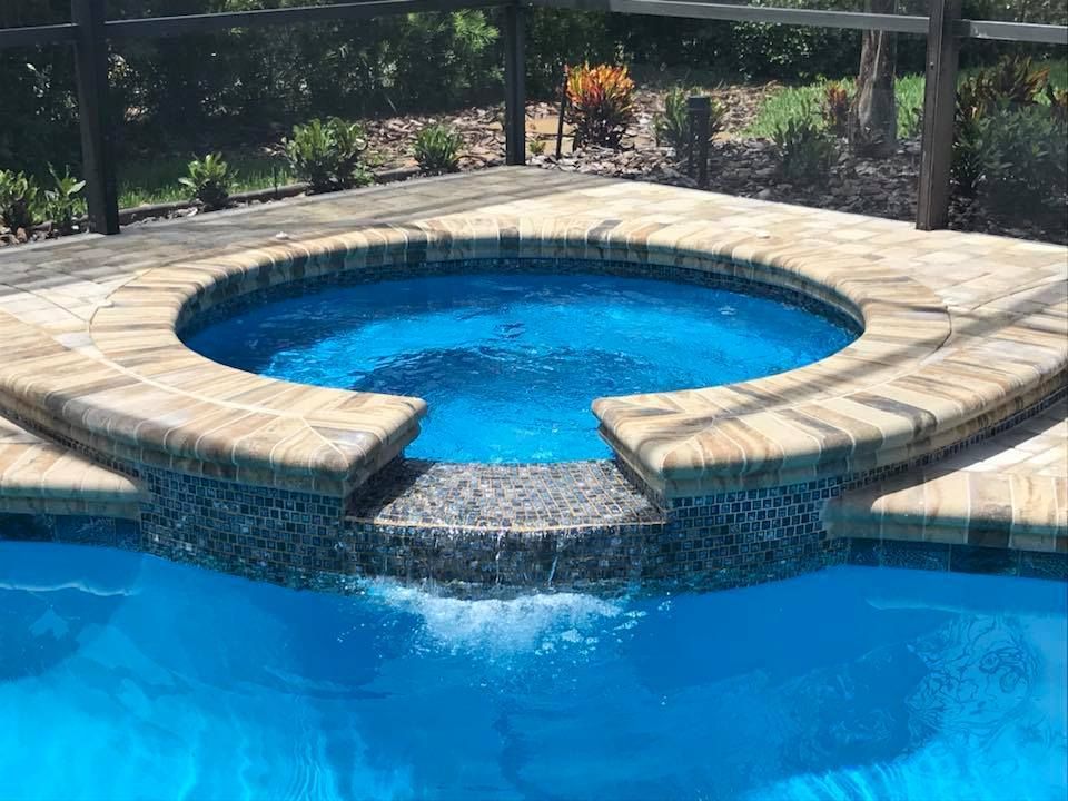 Blue pool with attached spa, water cascading from spa into pool.