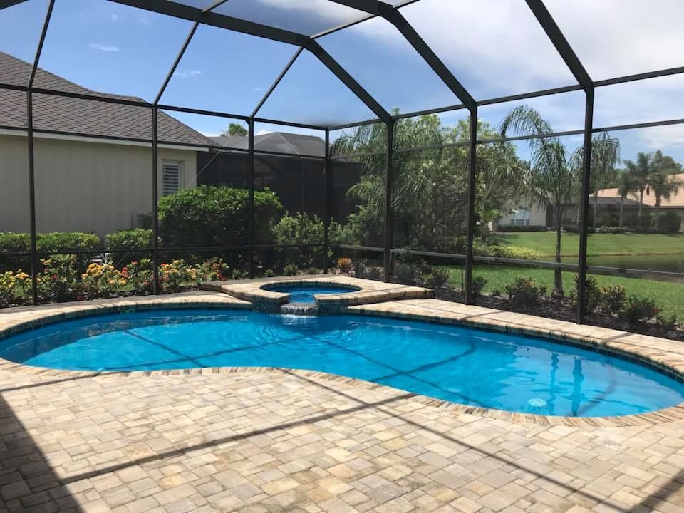 Swimming pool and hot tub enclosed in a screened patio, brick patio. Blue water and sky.