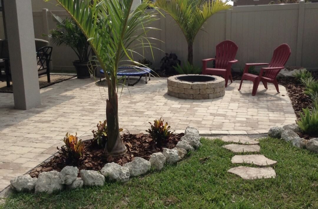 Patio with a stone fire pit, red chairs, palm trees, and landscaping.