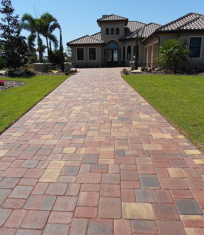 Brick driveway leading to a large house with a tower, blue sky, and green grass.