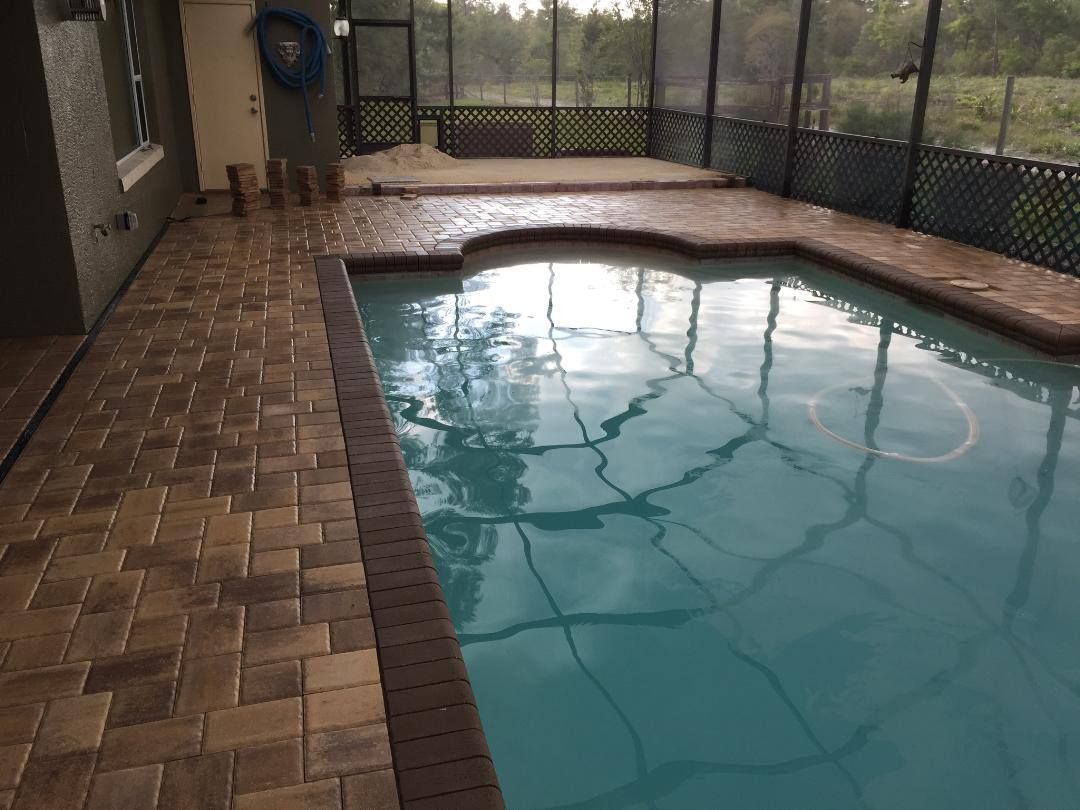 Pool with brick coping, screened enclosure, and natural landscape in background.