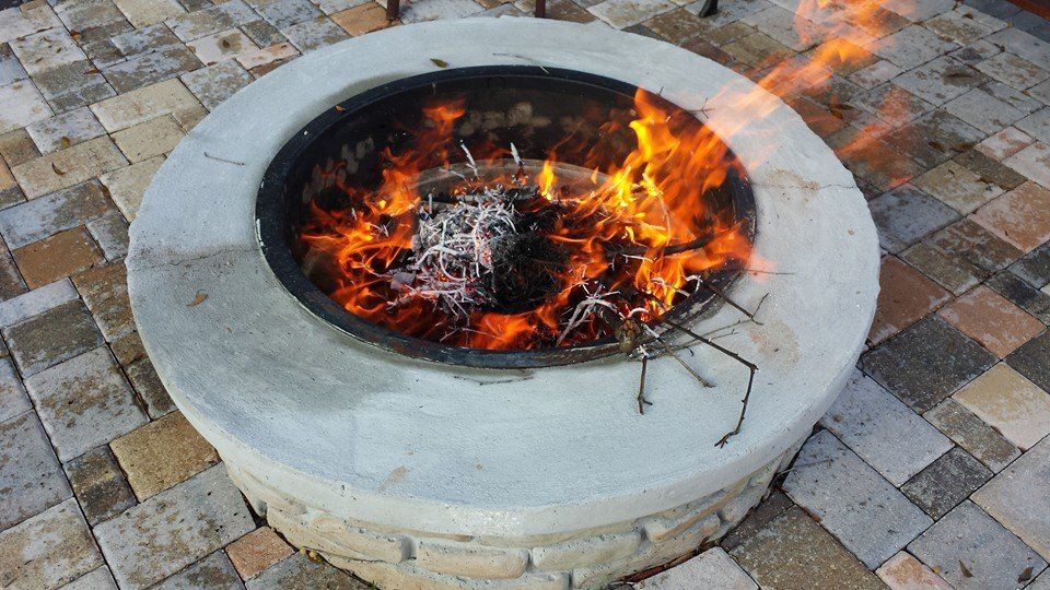 Fire pit burning brightly on a brick patio. Flames rise from wood and debris.