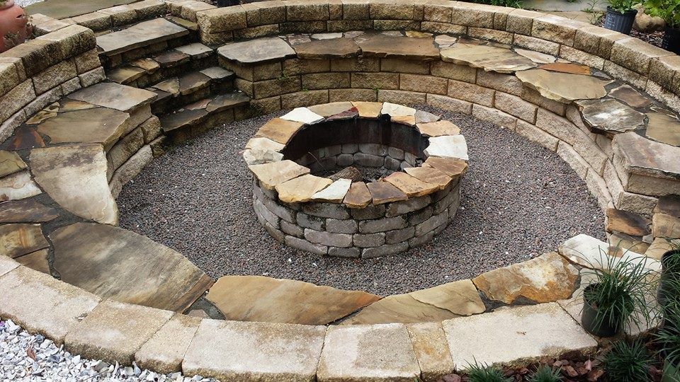 Stone fire pit with built-in seating. Circular design with stone steps and gravel base.