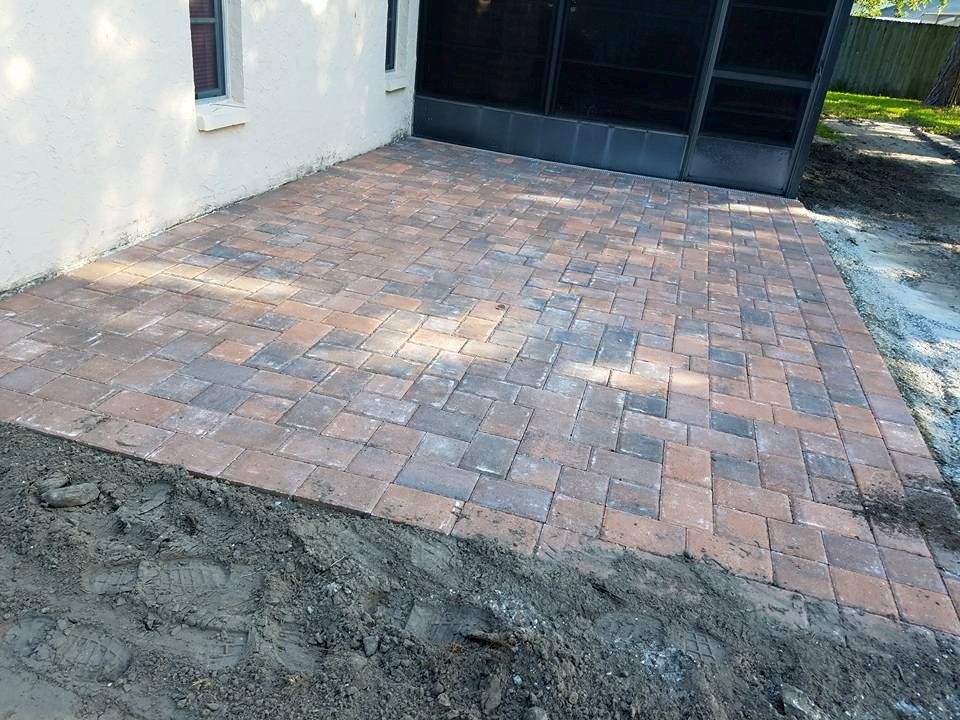 Brick patio outside a house next to a screened enclosure; reddish-brown and gray bricks.