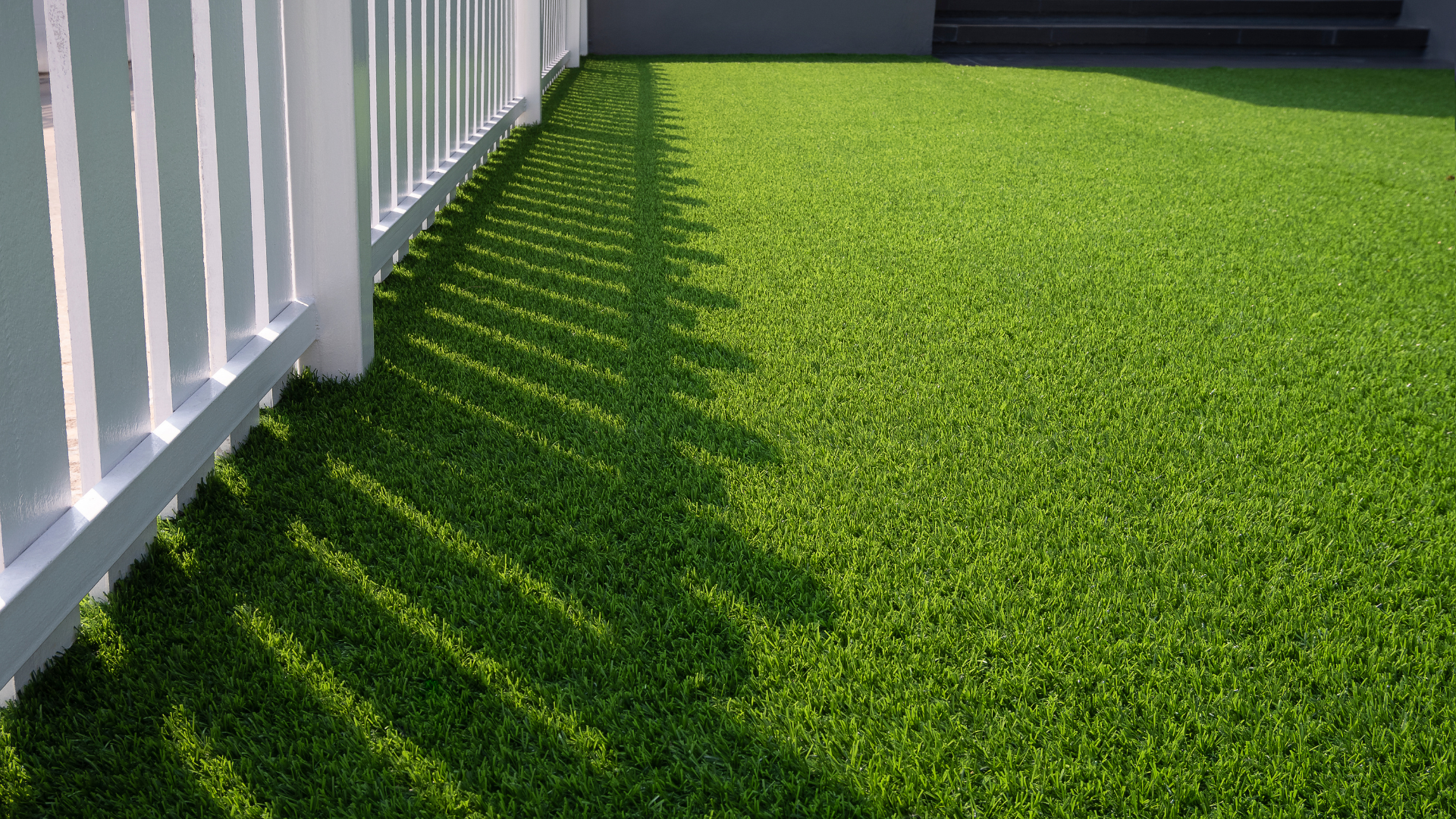 White fence casting shadows on bright green artificial turf.