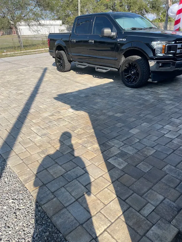 Black Ford pickup truck parked on brick pavers; shadow of a person.