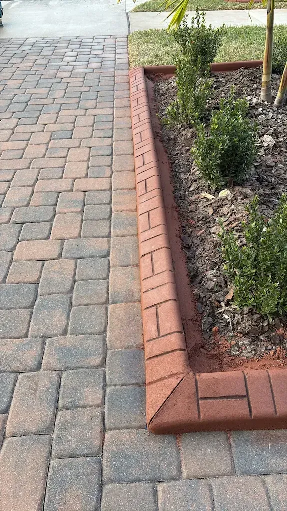 Brick walkway bordered by raised brick-lined planter with shrubs.