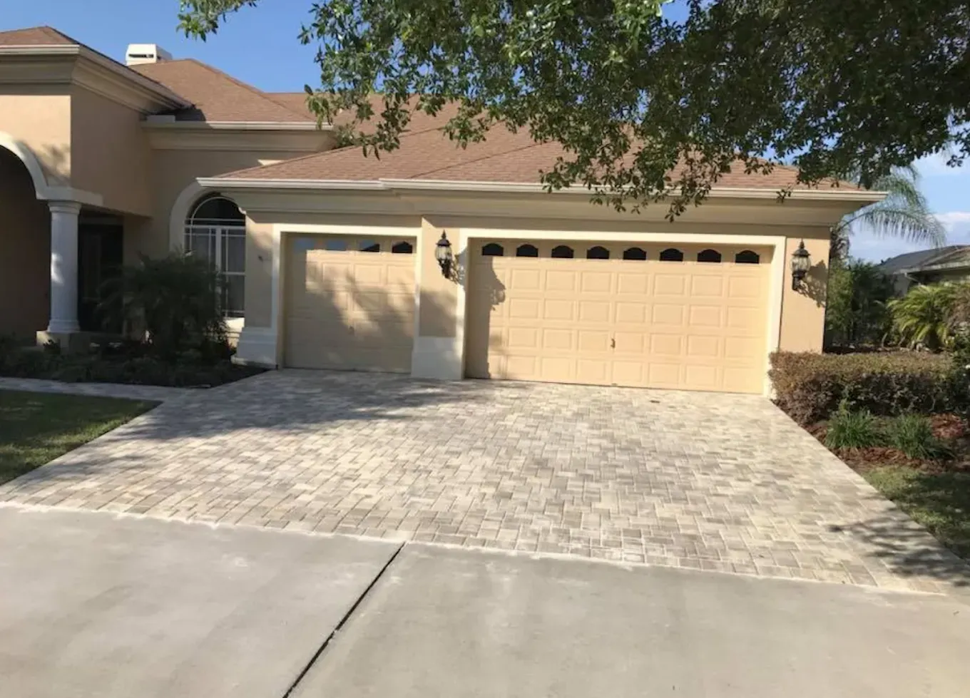 Tan house with brick-paved driveway leading to a two-car garage. Overcast sky.