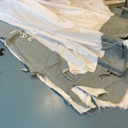 Hand holding a black clasp connected to green fabric with white stitching.